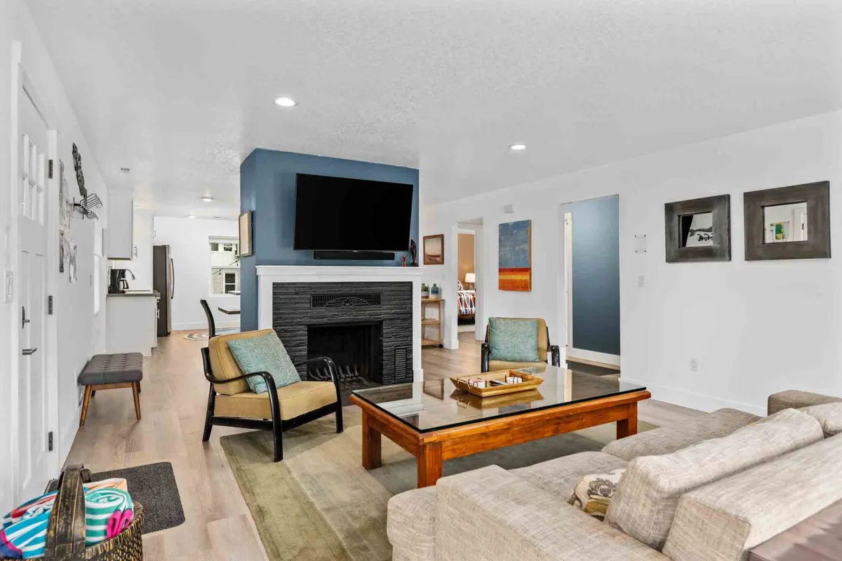 A comfortable living room setup featuring a decorative fireplace, a plush sofa, coffee table, and a wall-mounted television. Sunlight streams in, brightening the space and accentuating the cozy ambiance, making it ideal for relaxing, watching TV, or socializing.