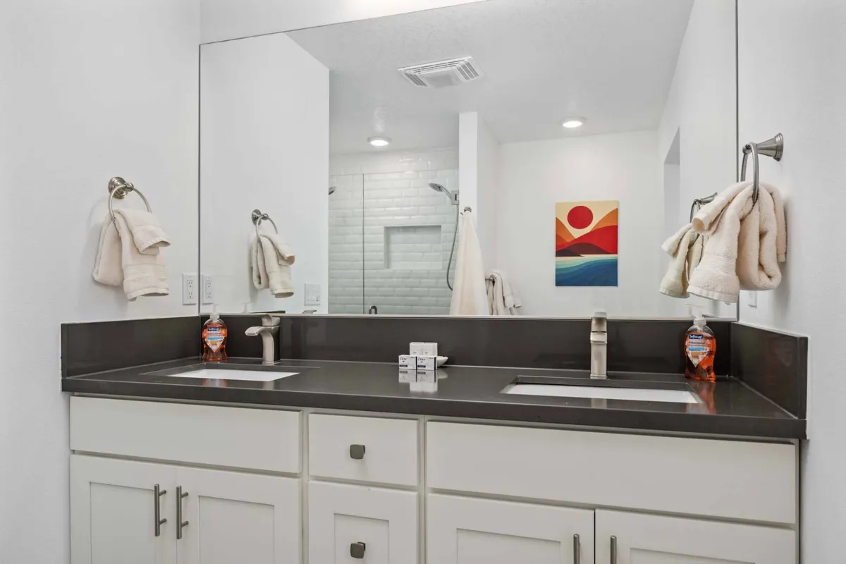 A contemporary bathroom featuring dual sinks, a large mirror above, and framed artwork on the wall. The space is bright and inviting, filled with morning light, and designed for comfort and convenience during daily routines.