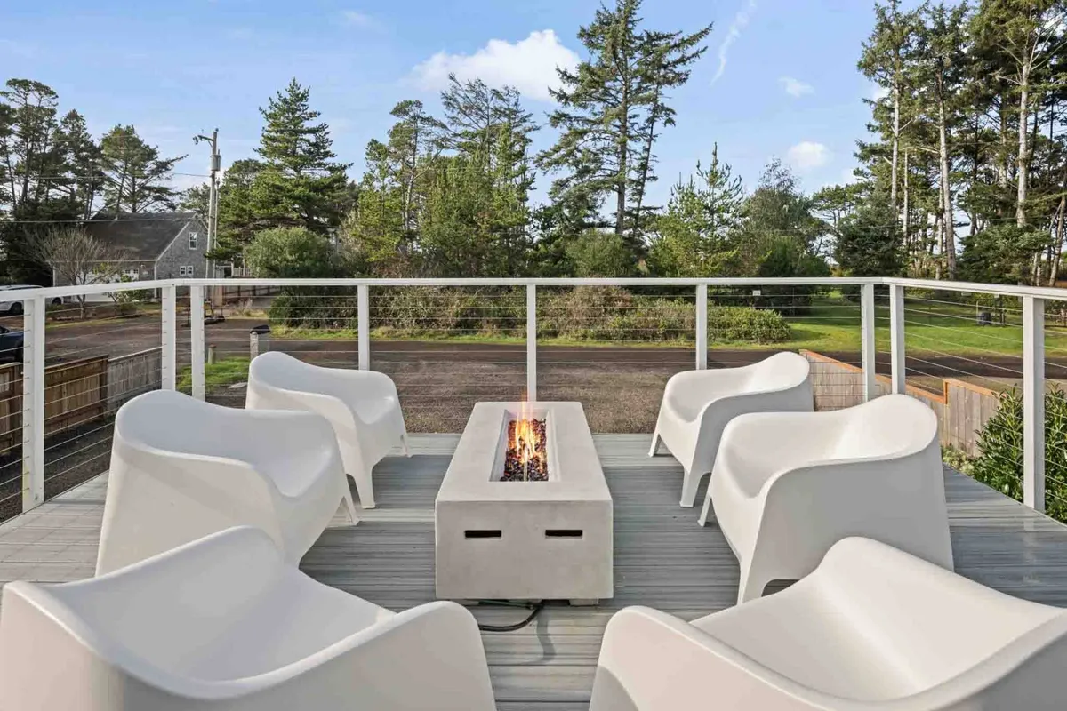 A cozy fire pit area with modern chairs is set amidst vibrant greenery. The arrangement invites guests to gather around the fire for intimate conversations, s’mores, or simply enjoying the warmth as the sun sets. The natural surroundings enhance the sense of an outdoor oasis.