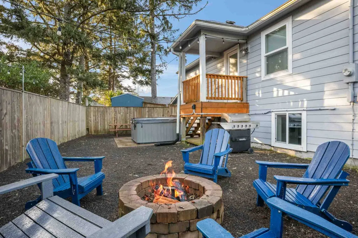 An exterior view featuring a deck with a fire pit surrounded by blue chairs. The setup is perfect for friends to gather, share stories, or enjoy a sunset. The mood is cozy and communal, inviting guests to make memories outdoors.