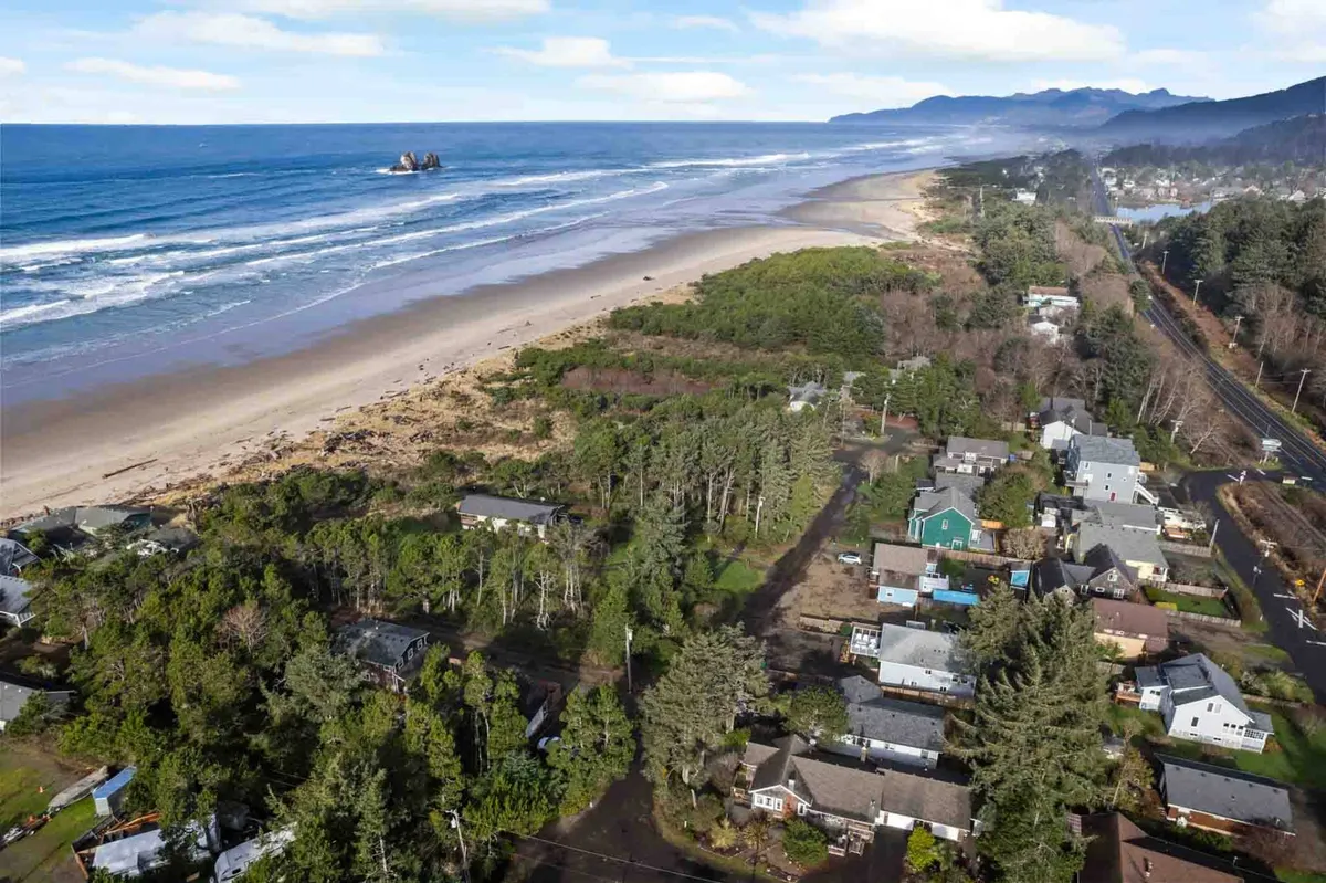 A sweeping view of the local beach and surrounding landscape, with ocean waves, rocky formations, and forested areas visible. This image captures the proximity of the home to natural attractions and the opportunities for seaside walks and sunset watching.