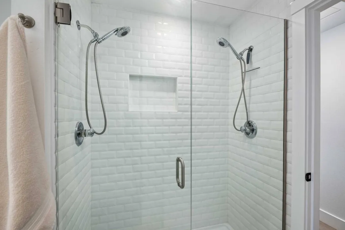 A modern bathroom with a glass shower enclosure, pristine white tiled walls, and gleaming fixtures. The space feels refreshing and serene, designed for invigorating showers or soothing baths.