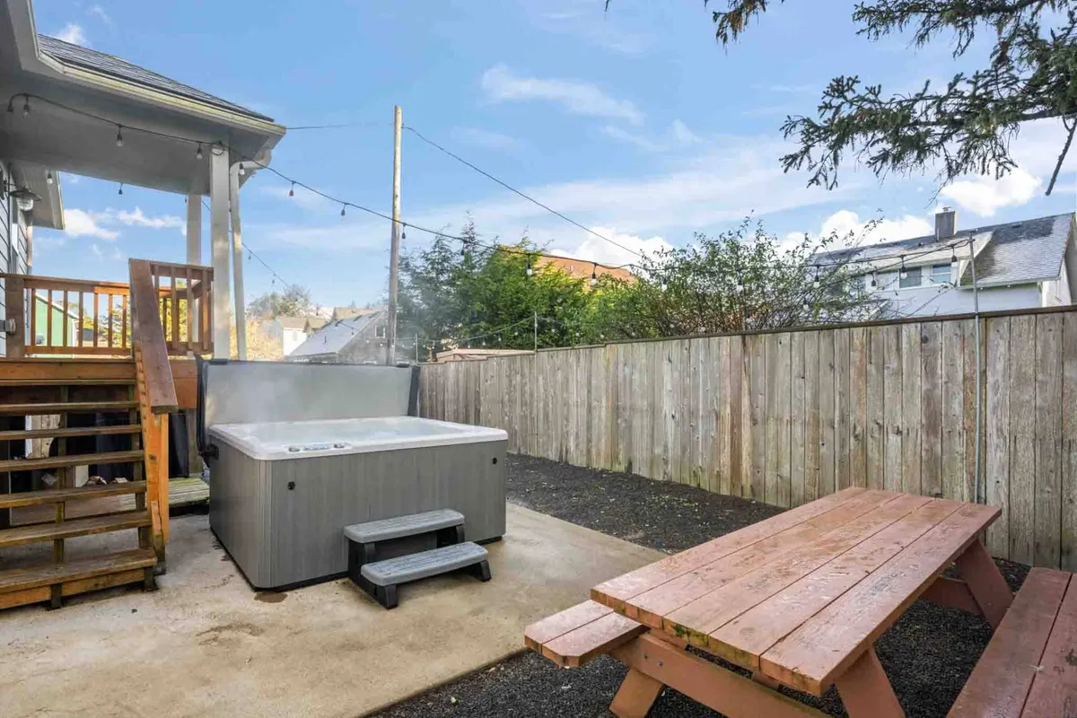 An outdoor area with a hot tub, picnic table, and wooden stairs, creating a versatile space for both relaxation and group dining. The scene suggests opportunities for enjoying sunset views, starlit nights, and shared laughter outdoors.