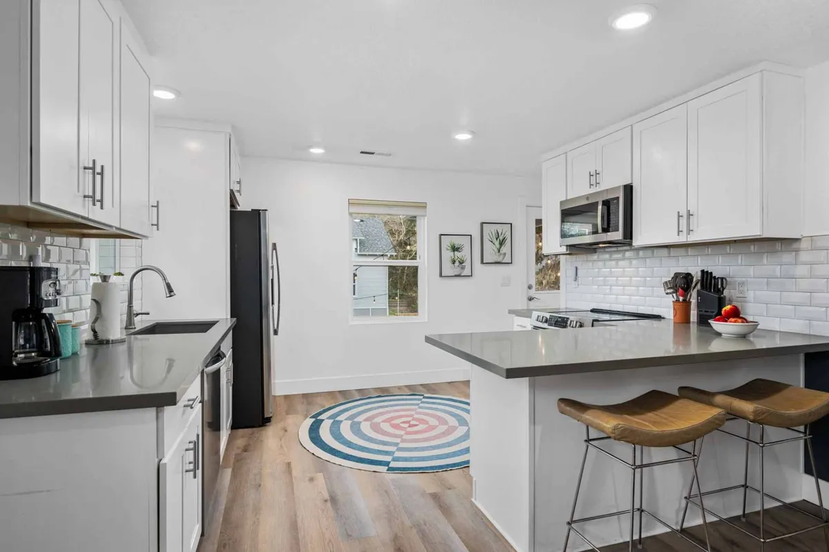 A cheerful kitchen scene with a kitchen island, colorful rug, stainless steel appliances, and decorative wall art. The space feels lively and ready for group cooking, entertaining, or family recipe creation.