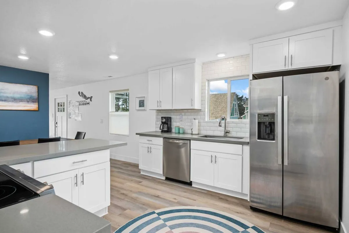A spacious, contemporary kitchen featuring a prominent kitchen island, stainless steel appliances, white cabinetry, and a striking blue accent wall. The area is bright and open, ideal for cooking and socializing, with thoughtful decor like a round rug adding a touch of comfort.